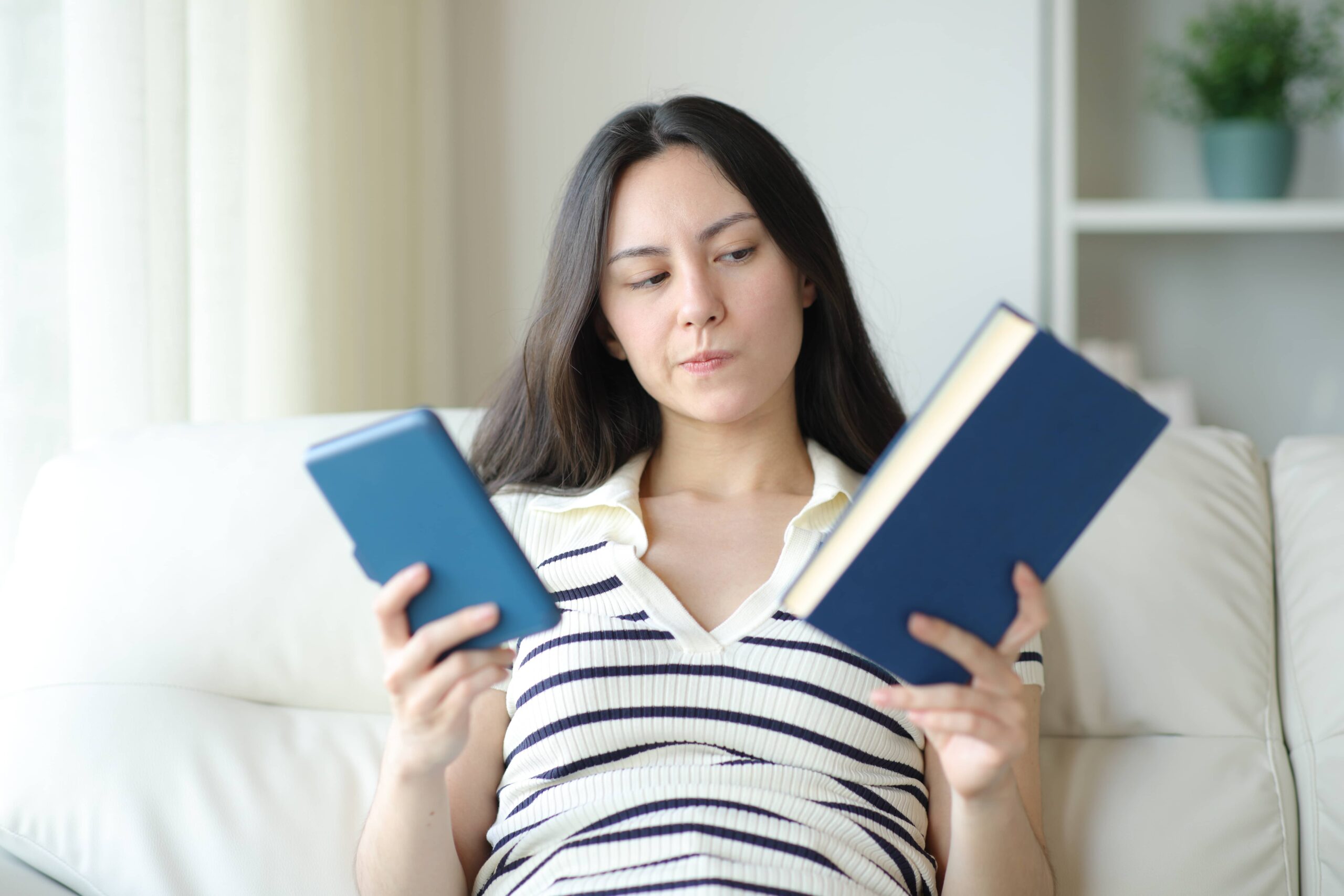 A girl looking undecided, holding a book and a Kindle in her hands